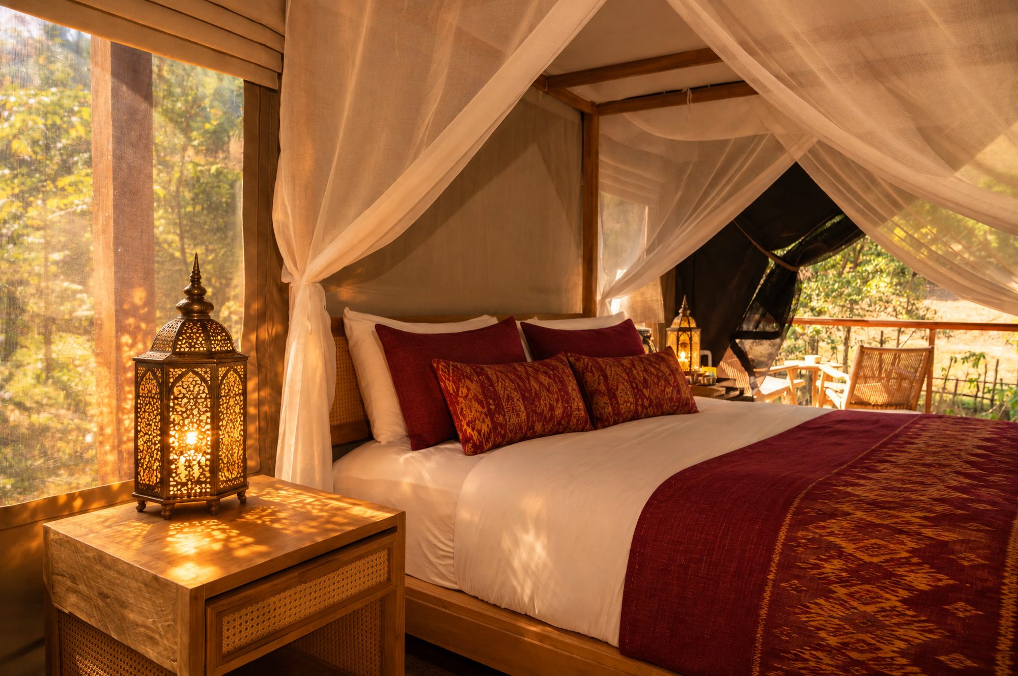 A luxury tent with red Khmer silk on the bed and a pierced brass lantern